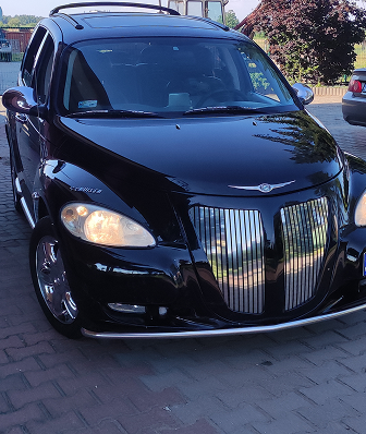 Black Chrysler PT Cruiser with a custom bumper and large chrome grille, parked outdoors.